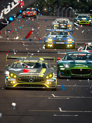 A photograph of seven race cars on a sunny day. Confetti fills the air as the cars approach the finish line.