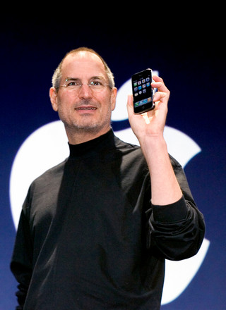 Steve Jobs on stage holding up the original iPhone
